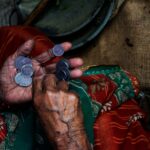 Close-up of an elderly woman's hands counting coins on a colorful textile background.